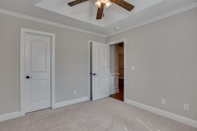 unfurnished bedroom with ceiling fan, light colored carpet, ornamental molding, and a tray ceiling