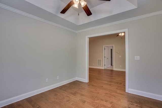 empty room featuring ceiling fan, ornamental molding, a tray ceiling, and light hardwood / wood-style flooring