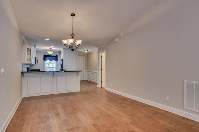 kitchen with pendant lighting, refrigerator, kitchen peninsula, white cabinetry, and a chandelier