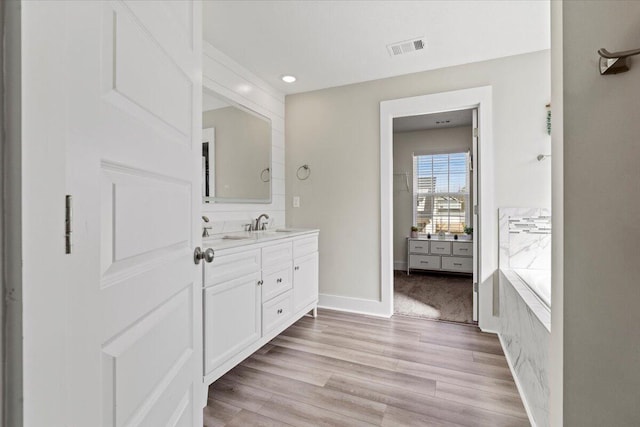 full bathroom with visible vents, a bathing tub, wood finished floors, baseboards, and vanity