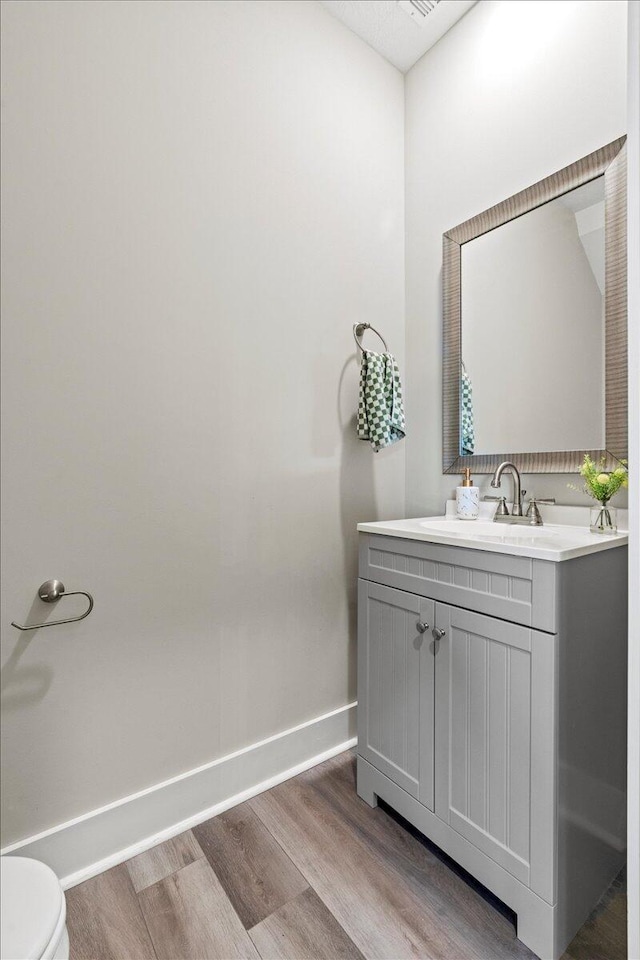 half bath featuring vanity, toilet, wood finished floors, and baseboards