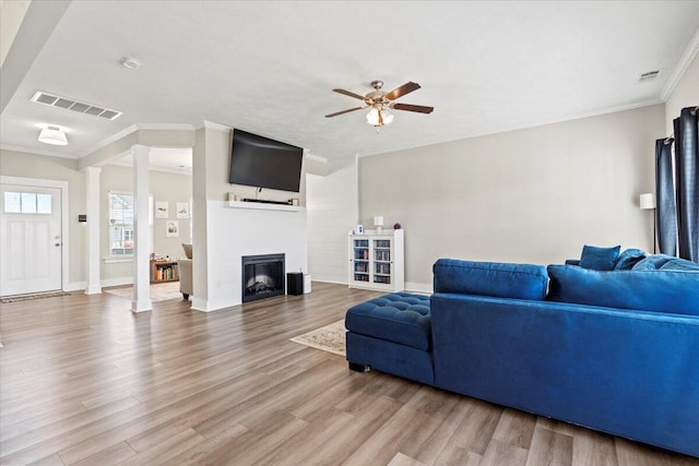 living room with crown molding, a fireplace, visible vents, and light wood finished floors