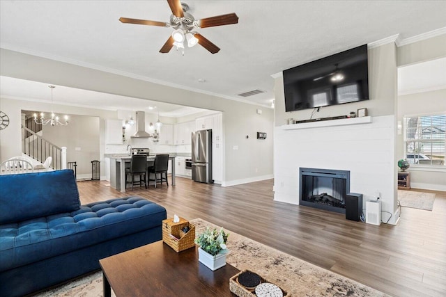 living room with a glass covered fireplace, visible vents, wood finished floors, and ornamental molding