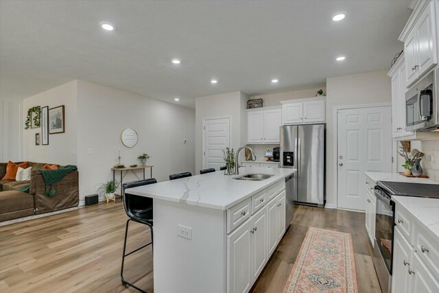 kitchen featuring appliances with stainless steel finishes, white cabinetry, light wood-style floors, and a sink