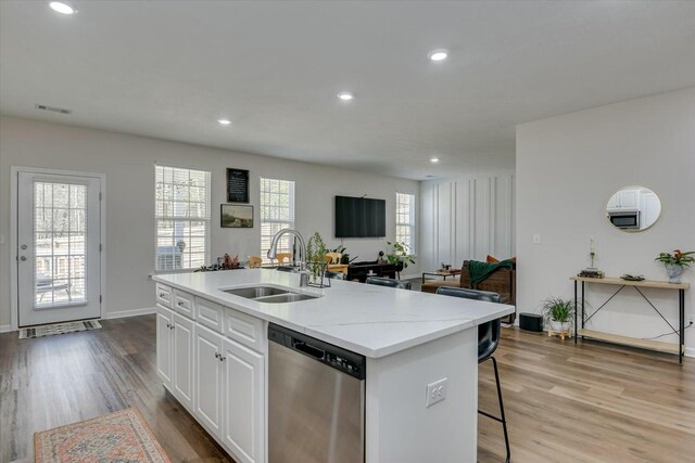 kitchen featuring stainless steel dishwasher, light wood-style flooring, an island with sink, and a sink