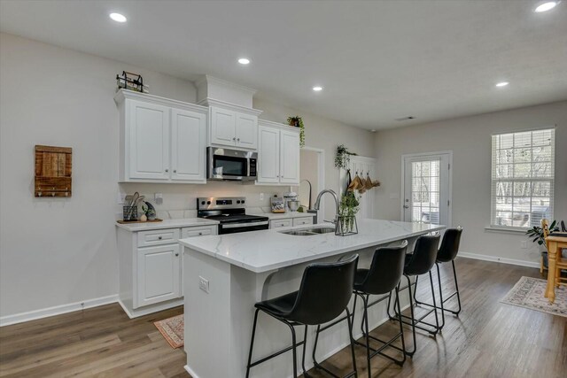 kitchen with appliances with stainless steel finishes, wood finished floors, a kitchen breakfast bar, and a sink