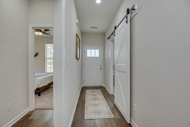 doorway with dark wood finished floors, visible vents, baseboards, and a barn door