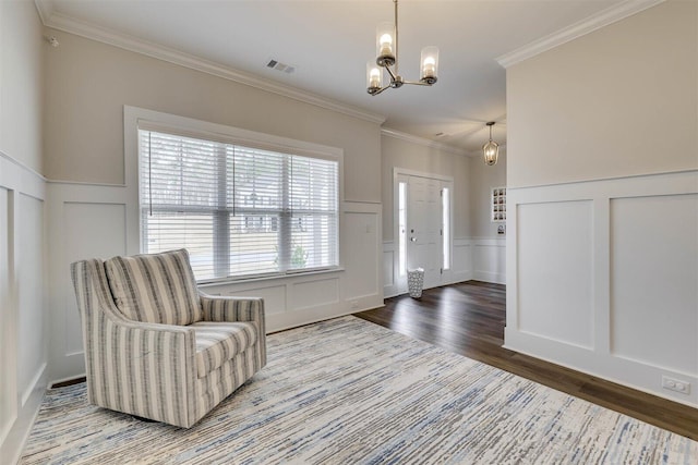 entrance foyer featuring visible vents, ornamental molding, wood finished floors, an inviting chandelier, and a decorative wall