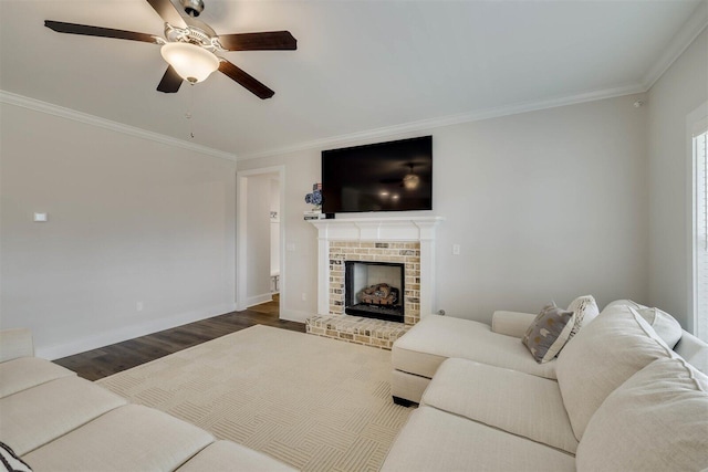 living room featuring dark wood finished floors, ornamental molding, a ceiling fan, a brick fireplace, and baseboards