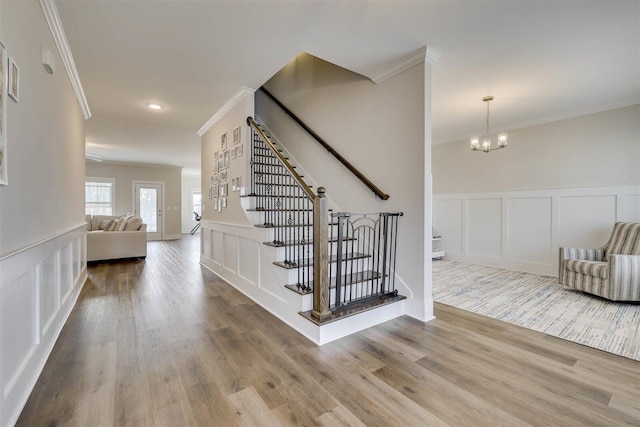 stairs with a wainscoted wall, a decorative wall, an inviting chandelier, ornamental molding, and wood finished floors