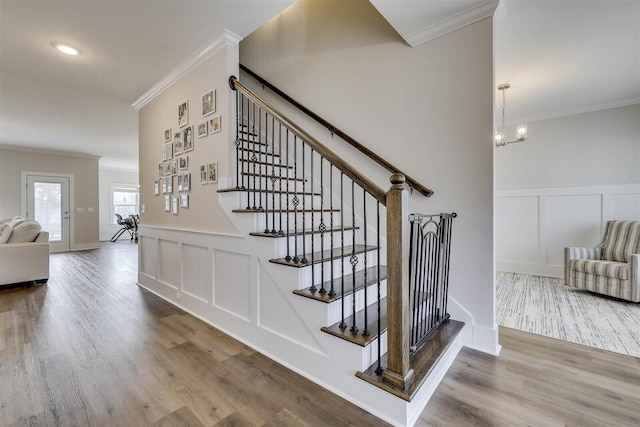 stairs featuring a notable chandelier, a decorative wall, ornamental molding, wainscoting, and wood finished floors