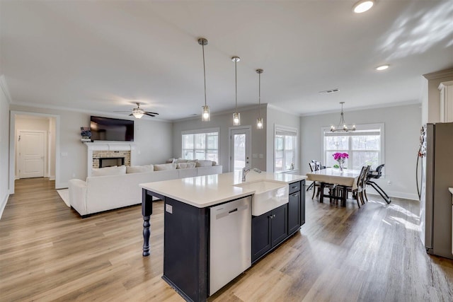 kitchen featuring open floor plan, hanging light fixtures, a kitchen island with sink, stainless steel appliances, and light countertops