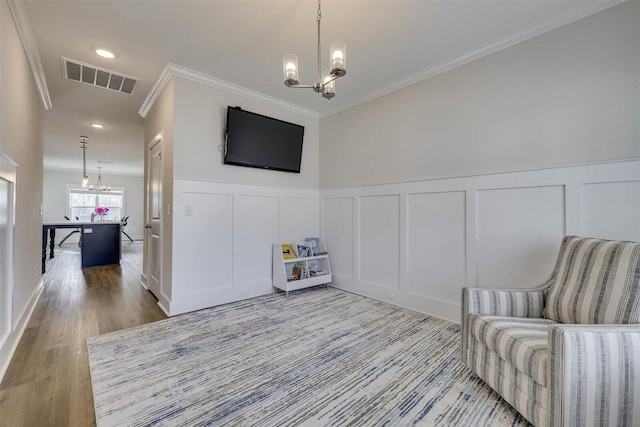 sitting room featuring a notable chandelier, visible vents, a decorative wall, ornamental molding, and wood finished floors