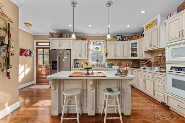 kitchen with a center island, white appliances, hanging light fixtures, light wood-type flooring, and ornamental molding