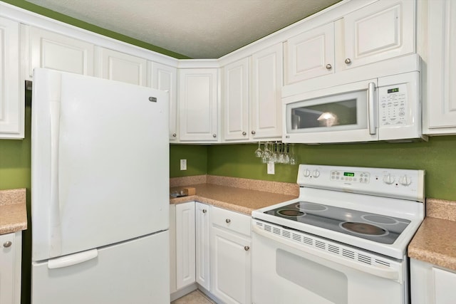 kitchen featuring a textured ceiling, white cabinetry, light countertops, and white appliances
