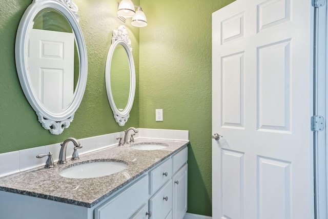 bathroom with a textured wall, double vanity, and a sink
