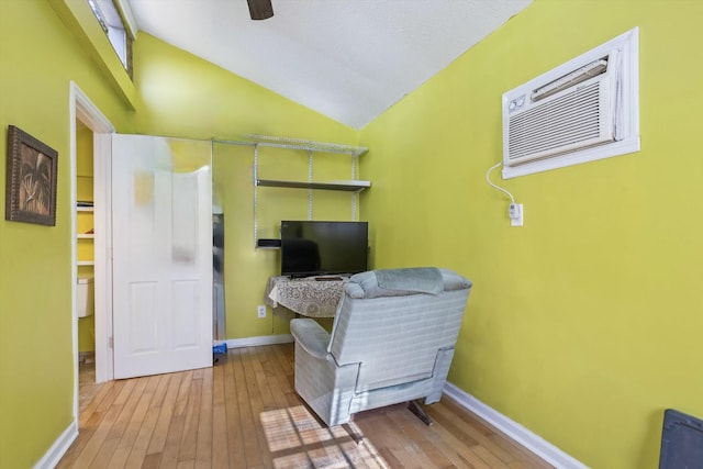 living area with a wall mounted AC, baseboards, vaulted ceiling, and hardwood / wood-style flooring