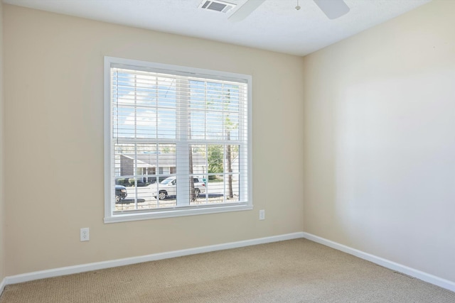 carpeted spare room featuring a healthy amount of sunlight, baseboards, a ceiling fan, and visible vents