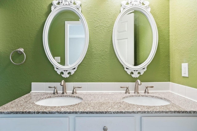bathroom featuring double vanity, a textured wall, and a sink