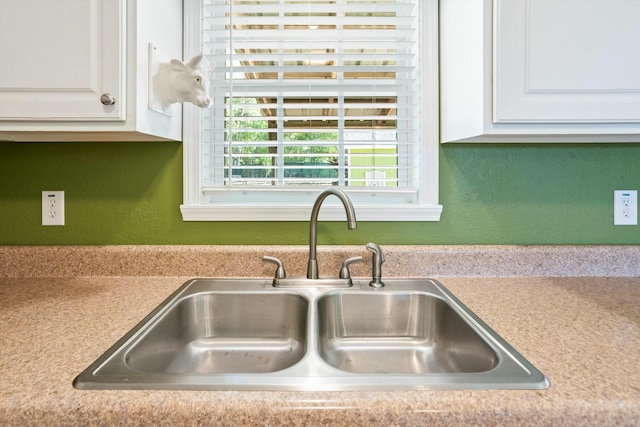 room details featuring a sink, light countertops, white cabinets, and a textured wall
