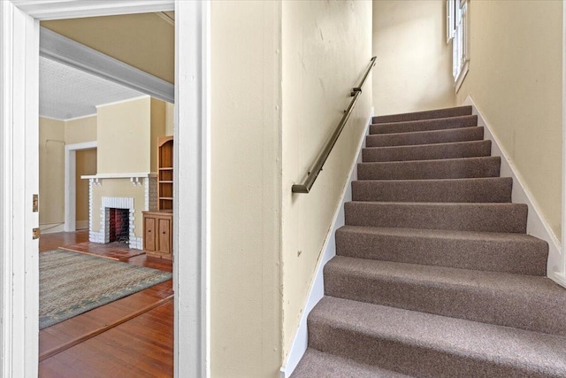 staircase featuring crown molding, a fireplace, and wood-type flooring