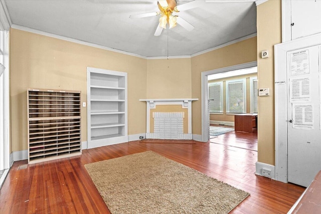 unfurnished living room with crown molding, a brick fireplace, built in shelves, ceiling fan, and dark hardwood / wood-style flooring