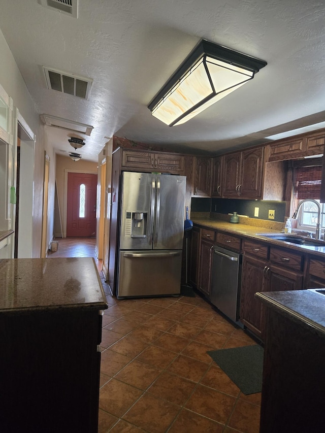 kitchen with stainless steel appliances, sink, a textured ceiling, dark brown cabinetry, and dark tile patterned floors