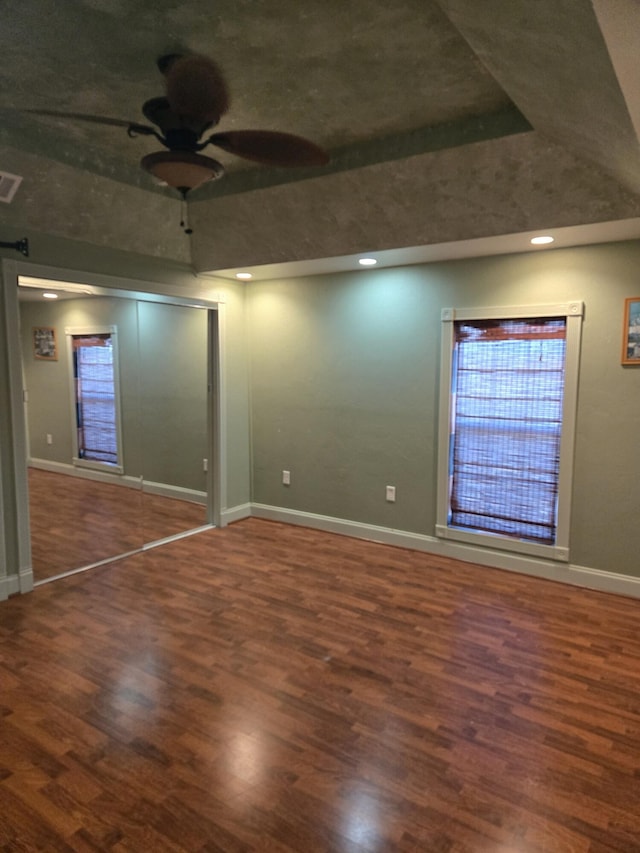 empty room featuring dark wood-type flooring, a raised ceiling, and ceiling fan