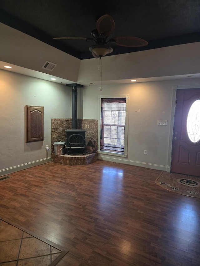 unfurnished living room featuring ceiling fan, a wood stove, and dark wood-type flooring