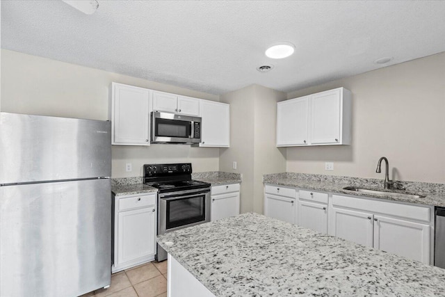 kitchen featuring light tile patterned floors, white cabinets, light stone countertops, stainless steel appliances, and a sink