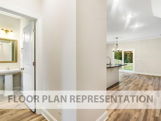 hallway with wood finished floors, baseboards, a chandelier, a sink, and crown molding