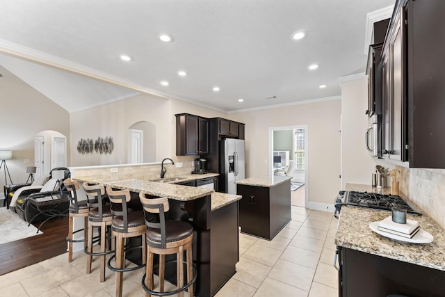 kitchen with sink, backsplash, stainless steel appliances, a center island, and light stone counters