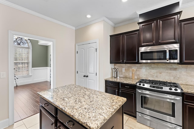 kitchen with stainless steel appliances, light tile patterned flooring, a kitchen island, and ornamental molding