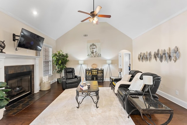 living room with lofted ceiling, dark wood-type flooring, ceiling fan, ornamental molding, and a tiled fireplace