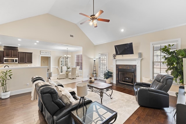 living room with a tile fireplace, ceiling fan with notable chandelier, lofted ceiling, crown molding, and dark wood-type flooring