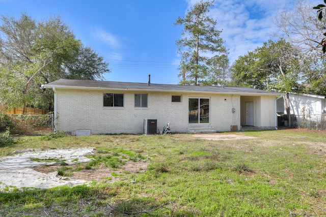 back of house featuring central AC unit, fence, brick siding, and a lawn