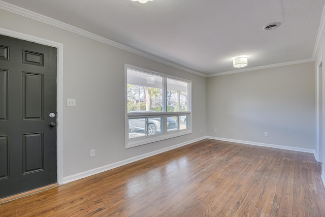 empty room with visible vents, wood finished floors, baseboards, and ornamental molding