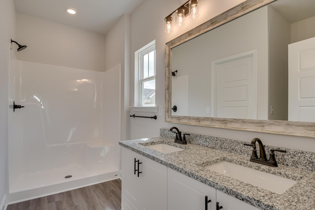 bathroom featuring double vanity, a walk in shower, wood finished floors, and a sink