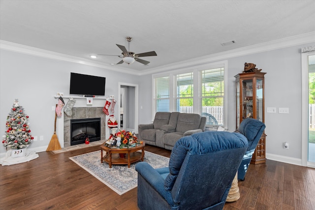 living room featuring ceiling fan, dark hardwood / wood-style floors, crown molding, and a tiled fireplace