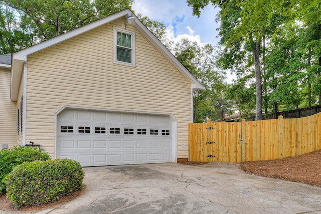 garage featuring concrete driveway, fence, and a gate