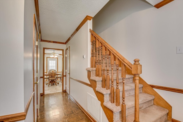 stairs featuring a ceiling fan, crown molding, a textured ceiling, visible vents, and baseboards