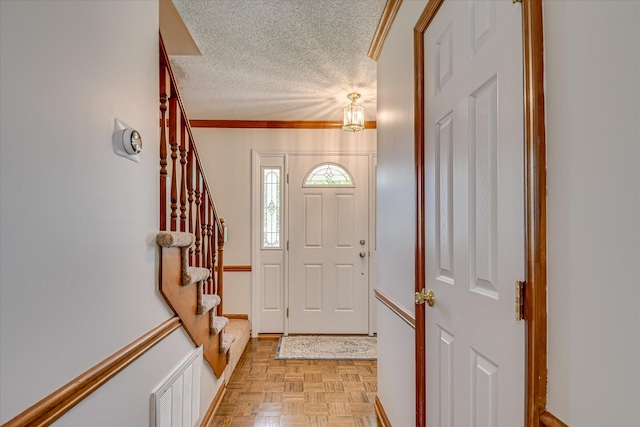 foyer featuring crown molding, a textured ceiling, visible vents, baseboards, and stairway