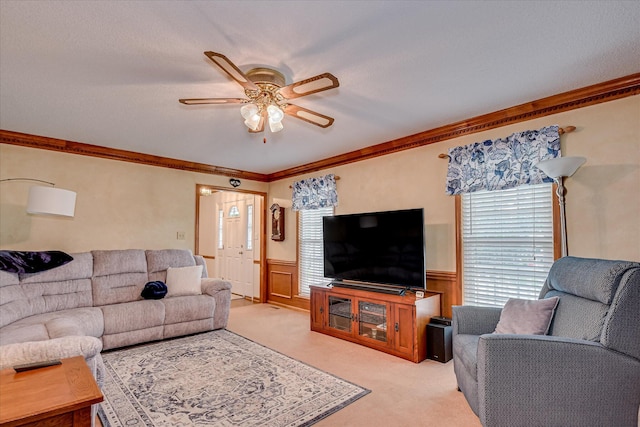 living area with wainscoting, light colored carpet, ornamental molding, and a ceiling fan