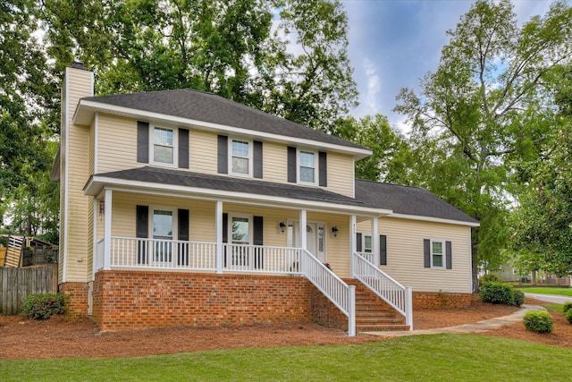 view of front facade with a porch, fence, a chimney, and a front yard
