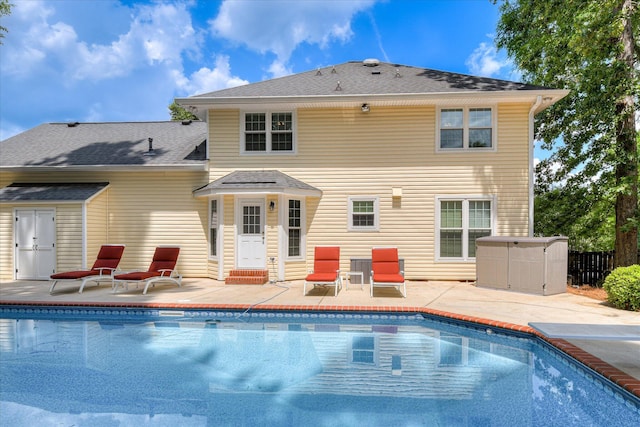 back of property featuring a patio, an outdoor pool, a shingled roof, and fence