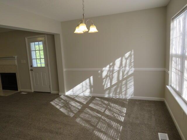 interior space with a notable chandelier, dark colored carpet, visible vents, a fireplace with flush hearth, and baseboards