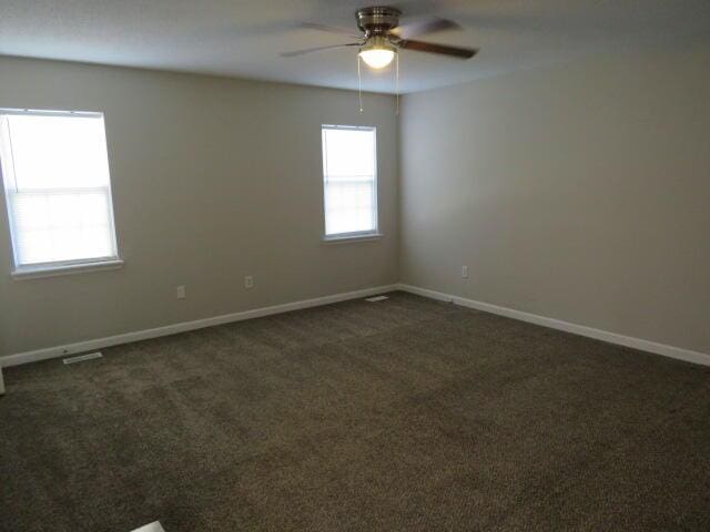 unfurnished room with a ceiling fan, dark colored carpet, and baseboards