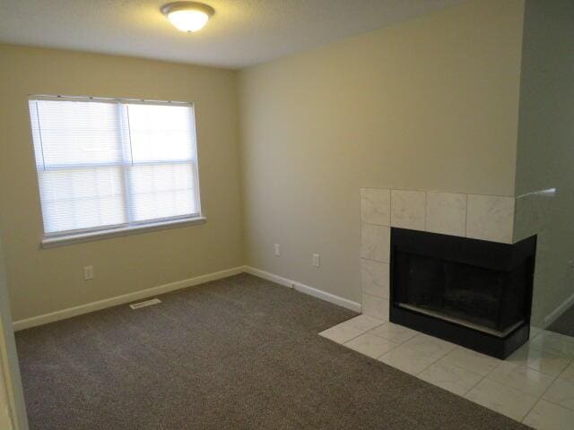 unfurnished living room with baseboards, carpet flooring, visible vents, and a tiled fireplace