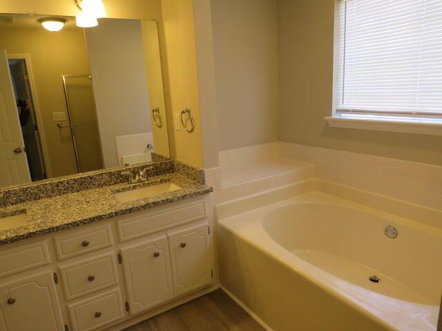 full bathroom featuring a garden tub, double vanity, wood finished floors, and a sink