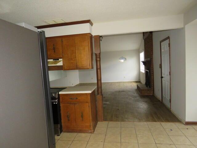 kitchen featuring brown cabinetry, freestanding refrigerator, light countertops, under cabinet range hood, and a fireplace